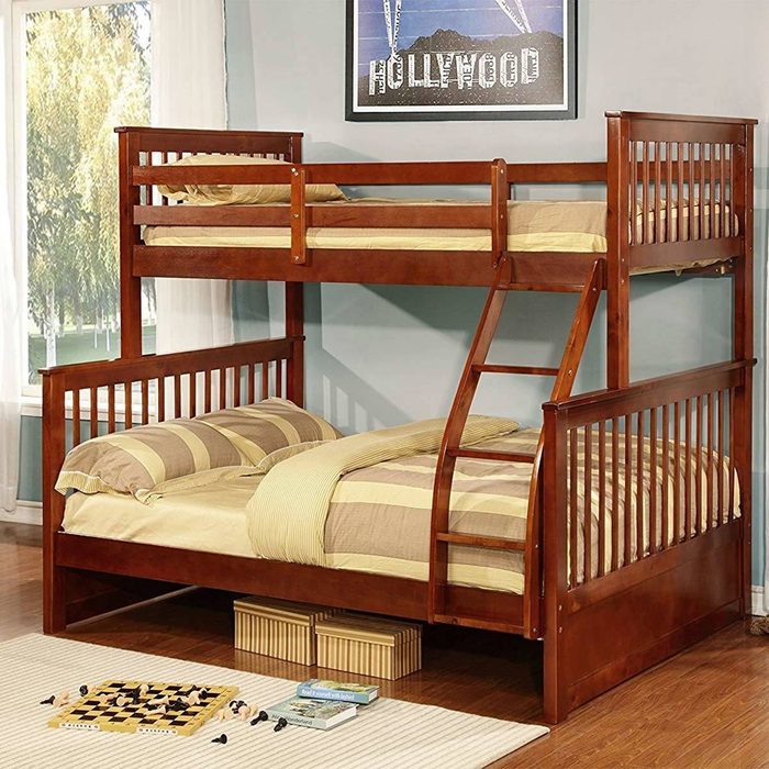 A wooden bunk bed occupies a room, with a top and bottom sleeping area. A ladder connects them, alongside a chess game and books on the floor.