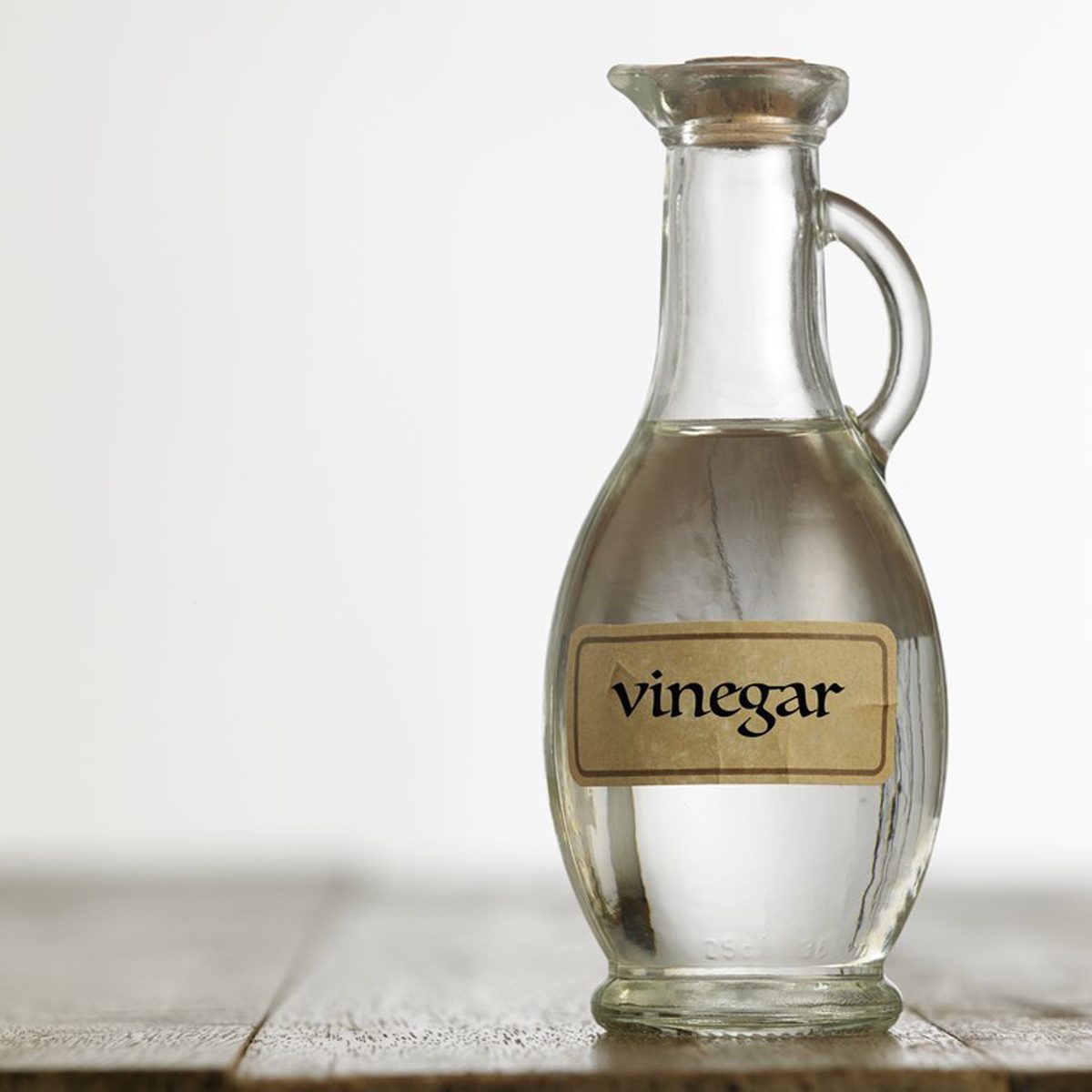 A glass bottle labeled "vinegar" stands upright on a wooden surface, reflecting light against a soft, neutral background.