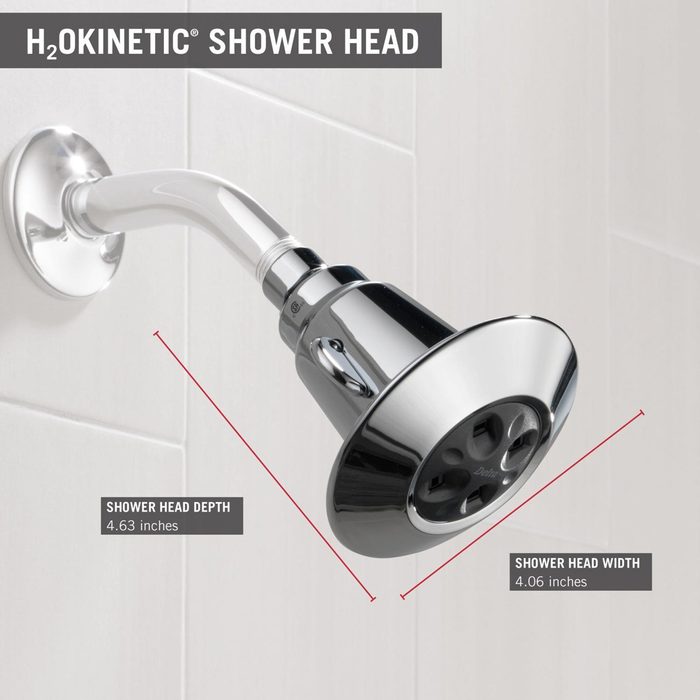 A chrome shower head is mounted on a wall, displaying measurements for depth and width, surrounded by smooth white tiles.
