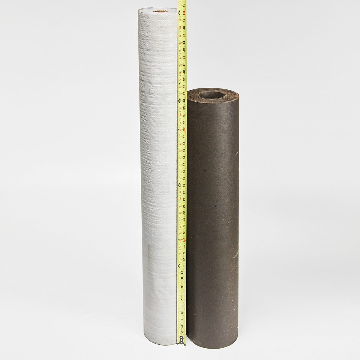 Two rolls of paper stand vertically, one white and one brown, with a measuring tape showing their heights against a plain white background.
