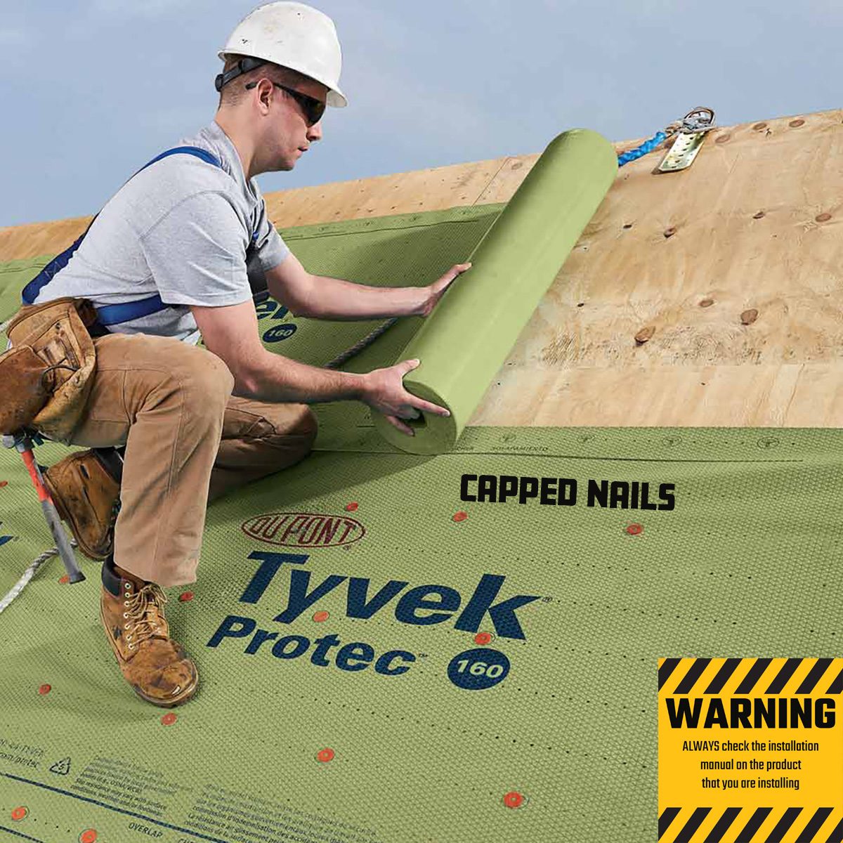A worker installs a green roll of Tyvek material on a wooden surface, with safety gear and a warning sign about installation precautions nearby.