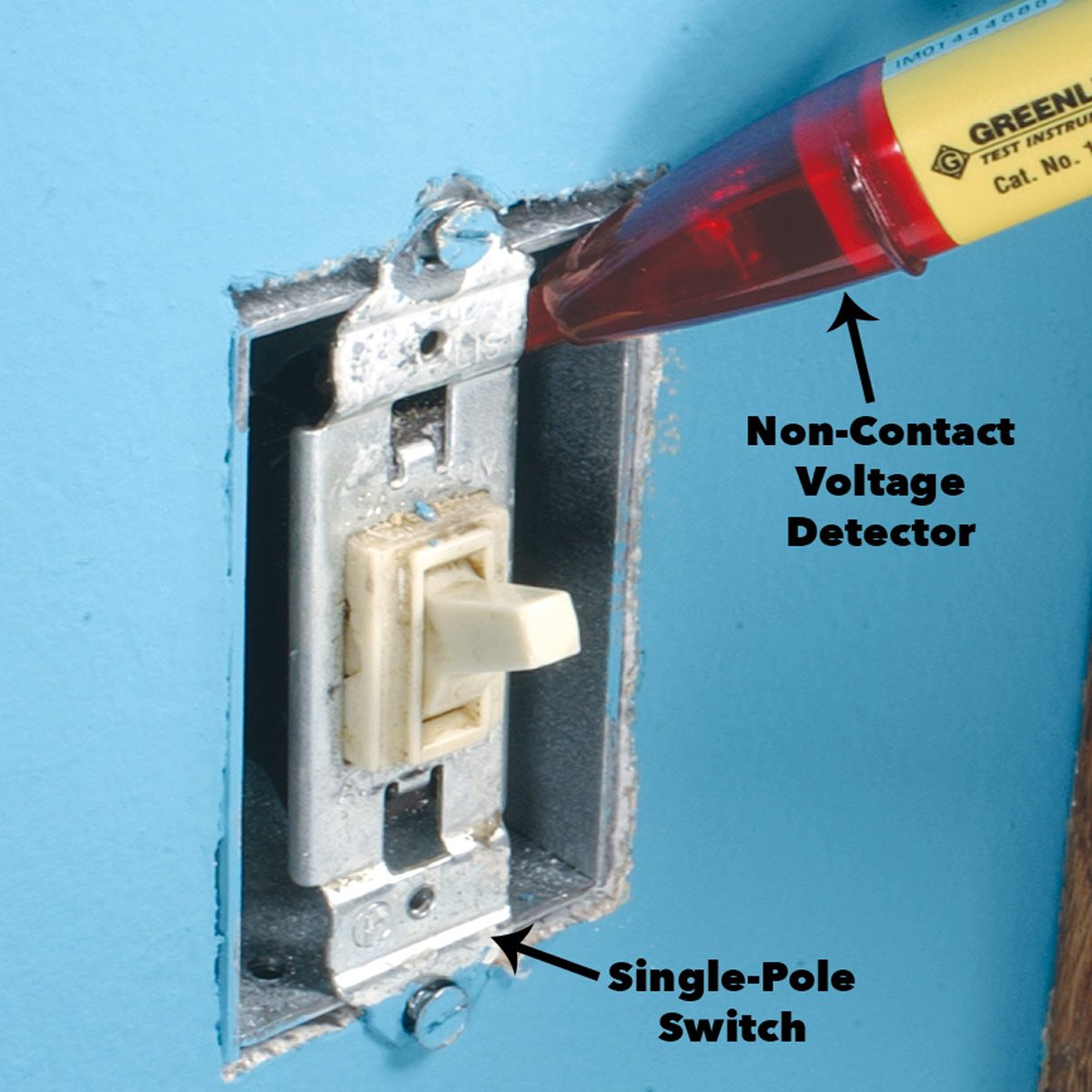 A non-contact voltage detector hovers near a single-pole switch, set against a blue wall, indicating an electrical testing scenario.
