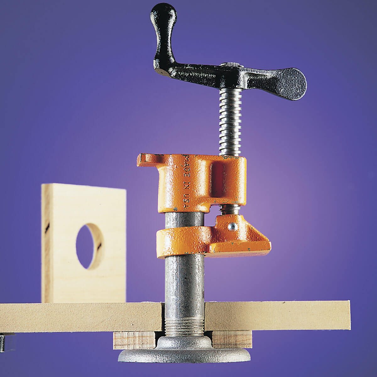 A clamp tightly secures two wooden pieces together. The background is a gradient of purple, emphasizing the tool's metallic and orange components.