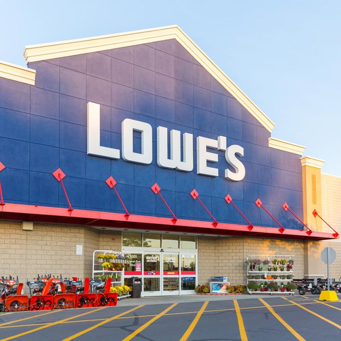 Storefront of Lowe's, featuring large signage; outdoor displays include planters and snow removal equipment; clear skies above and painted parking lot in front.