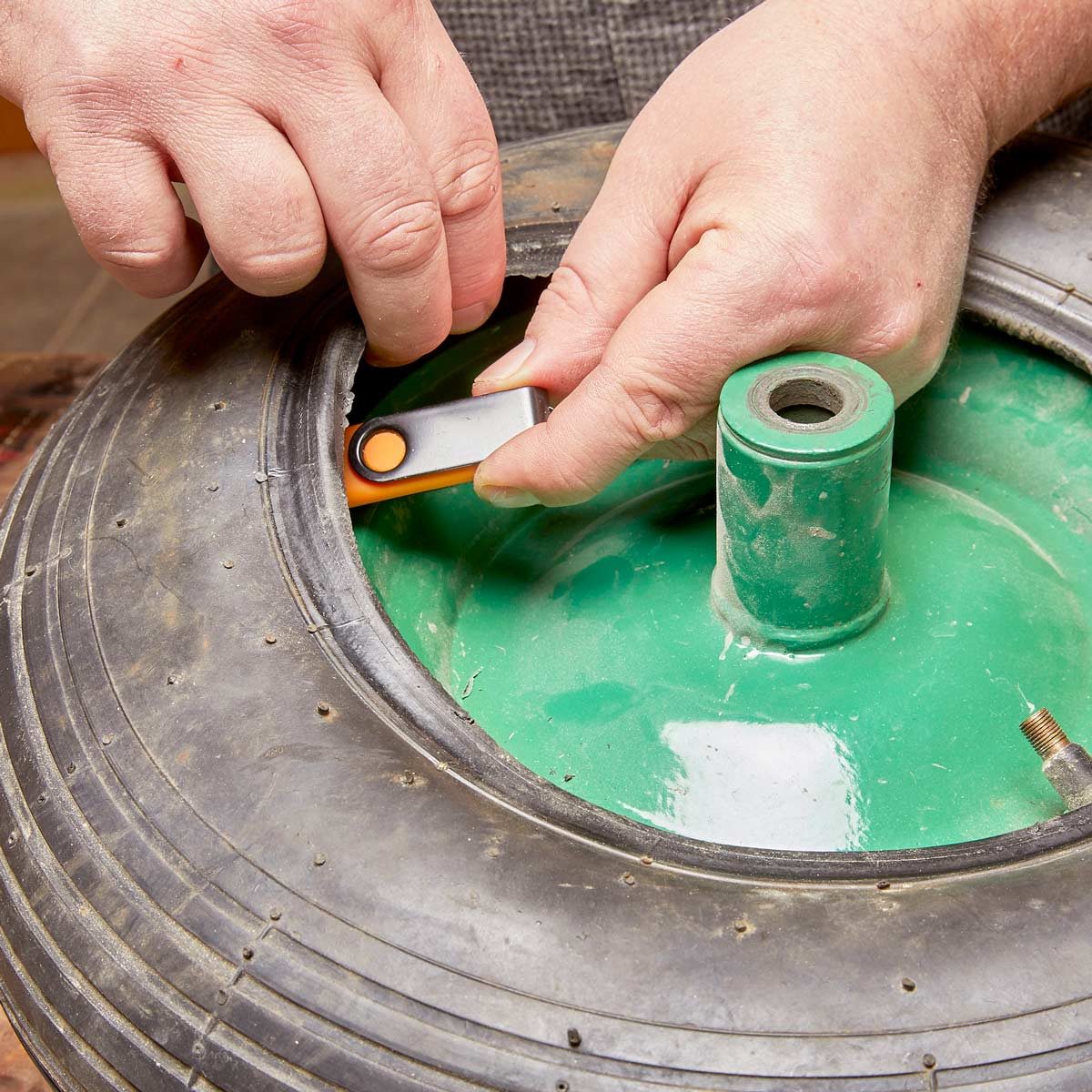 A person uses a tool to repair a tire, focusing on the inner rim of a green tire within a workshop setting.