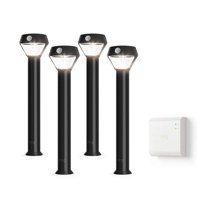 Four black outdoor path lights with triangular tops illuminate a setting, accompanied by a small white control unit on the right.