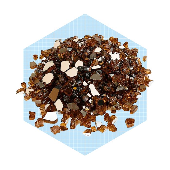 Brown crystalline particles are piled together on a light blue grid background, reflecting light and displaying various facets and shapes.