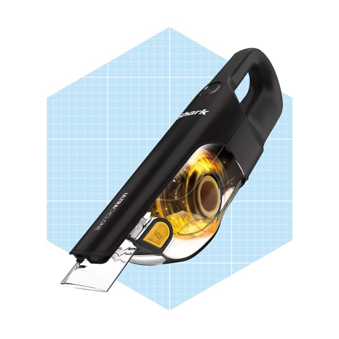 A handheld vacuum cleaner is positioned at an angle, featuring a transparent dust compartment. The background is a light blue grid pattern, emphasizing the object.