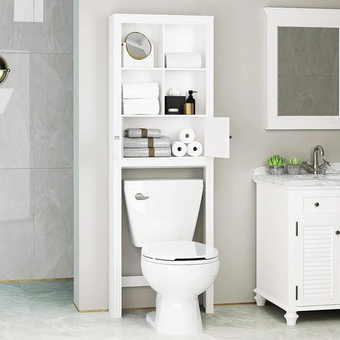 A white bathroom cabinet with shelves full of towels and toiletries stands above a white toilet, adjacent to a marble-top sink and a mirror.