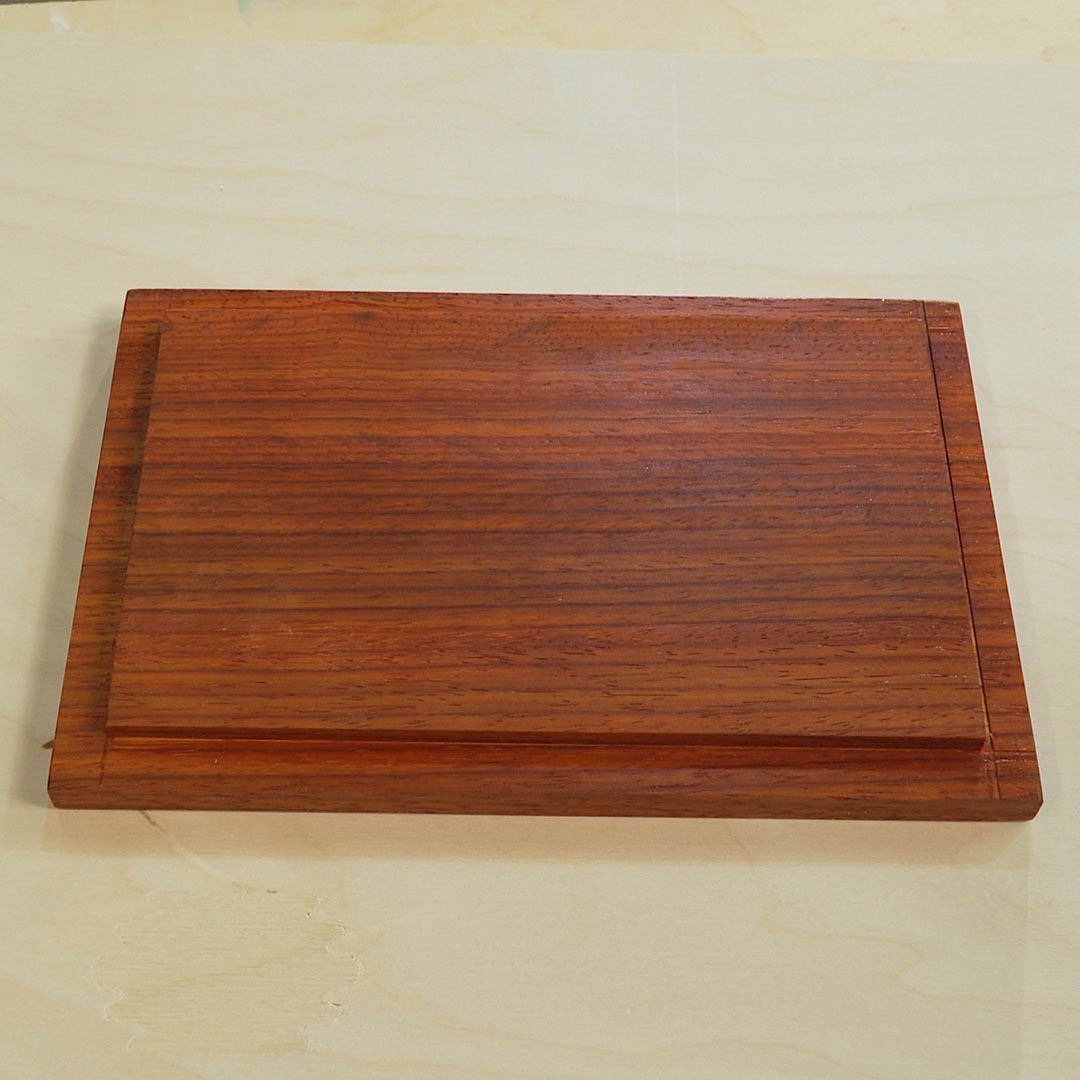 A wooden plaque rests on a light-colored surface, showcasing a smooth, polished finish with subtle grain patterns and a simplified rectangular shape.