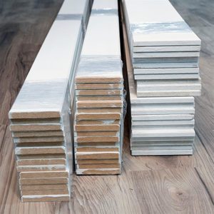 Long, stacked pieces of material sit side by side on a wooden floor, some wrapped in plastic, showcasing distinct layers and textures.