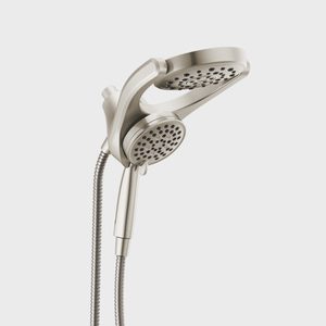 A metallic showerhead, attached to a flexible hose, is positioned upright, ready for use in a bathroom setting with a minimalist backdrop.