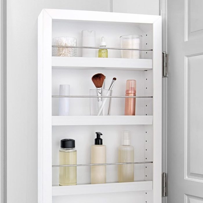 A white shelf displays various cosmetic containers, brushes, and tools, organized neatly in a bathroom setting, suggesting a space for personal care and grooming.