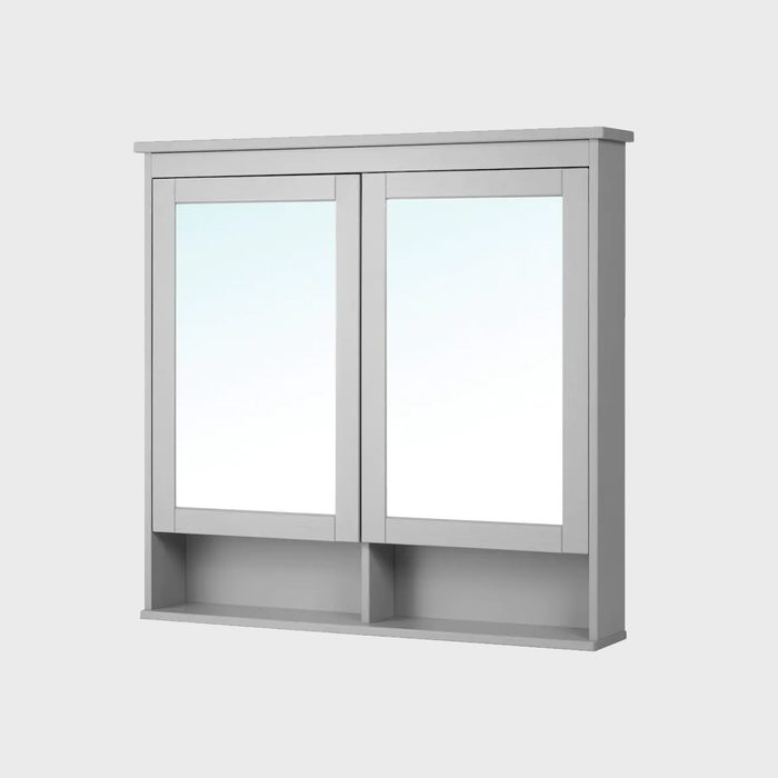A double mirror cabinet hangs on a wall, reflecting light. Below, a shelf provides space for storing items in a simple, modern design.