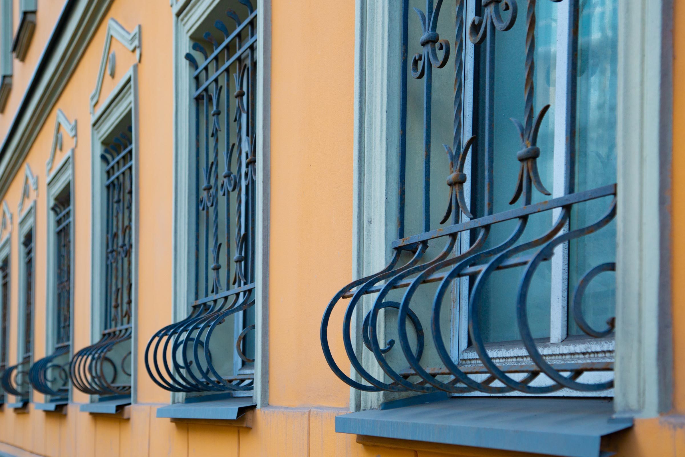 Decorative metal window bars adorn blue-tinged windows on a yellow wall, showcasing architectural detail in a building's exterior.