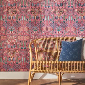 A rattan bench with a blue decorative pillow sits against a vibrant floral-patterned wallpaper, creating a cozy, inviting atmosphere in the room.