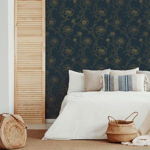 A bed is neatly arranged with pillows and a white blanket, next to a wooden screen, against a floral-patterned dark wall in a cozy room.