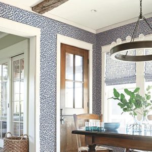 A wooden door stands against a patterned wall, while a dining table with glassware and a plant occupies the room, illuminated by a pendant light.