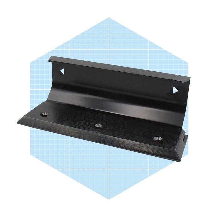 A black metal bracket is positioned for mounting, featuring three holes for screws, set against a light blue grid-patterned background.