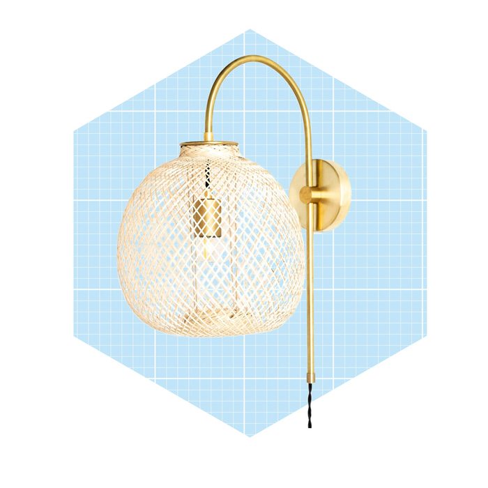 A pendant light, suspended from a wall, emits illumination. It features a woven design and a gold fixture against a blue grid background.