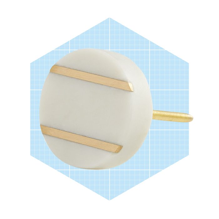 A round decorative pin with a white base and two horizontal gold stripes is positioned against a light blue geometric background.