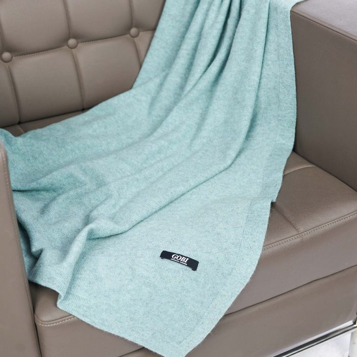 A soft, light blue blanket drapes over a section of a modern, beige leather couch, inviting warmth and comfort in a cozy interior setting.