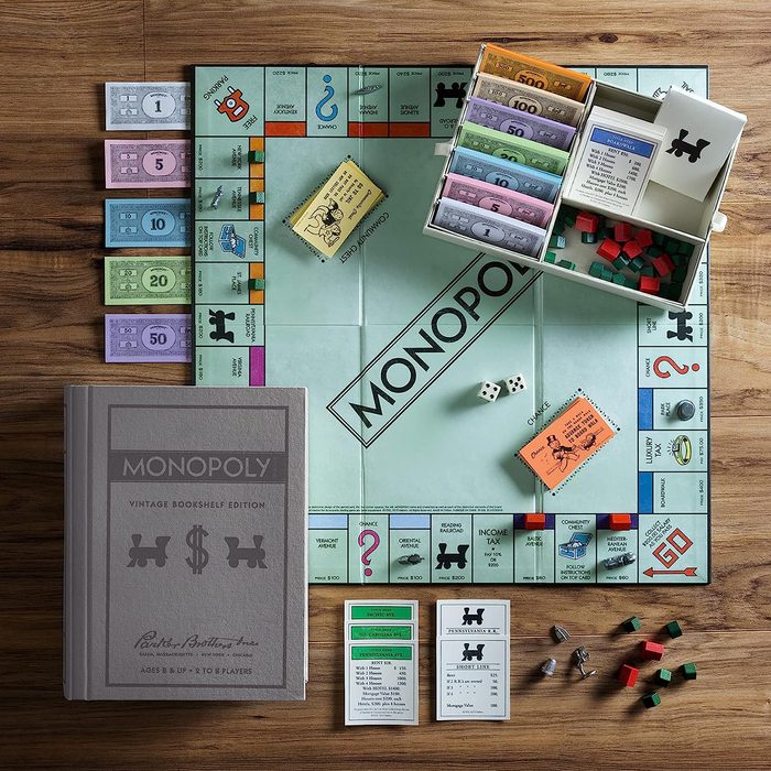 A Monopoly game is set up on a wooden table, featuring a board, dice, money, property cards, and game pieces in organized sections.