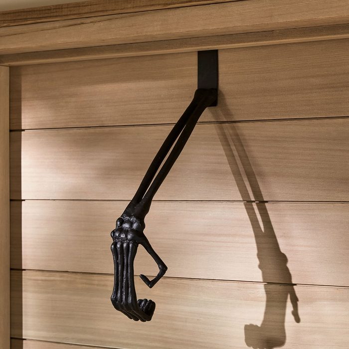 A black, skeletal hand hooks from a wall, casting a shadow against wooden panels, adding an eerie touch to the environment.