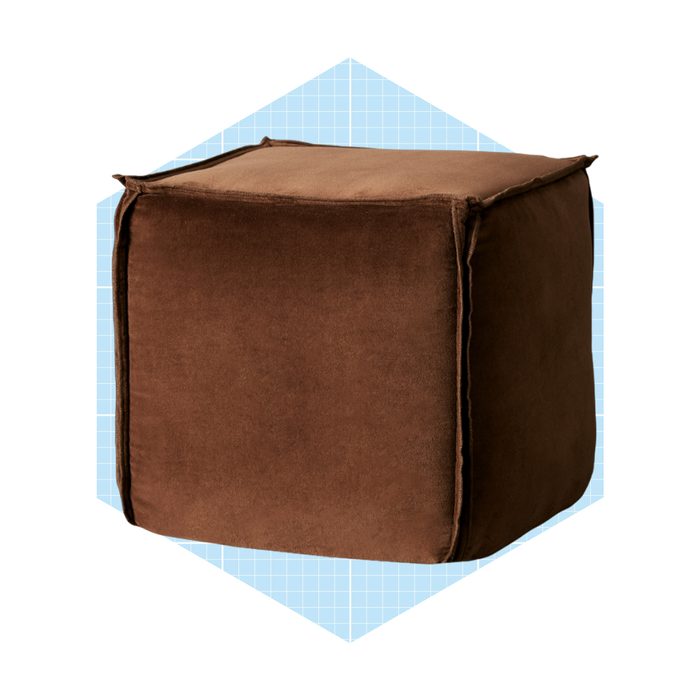 A brown, square pouf sits upright on a light blue, grid-patterned background. It is soft, with rounded edges and a smooth surface.