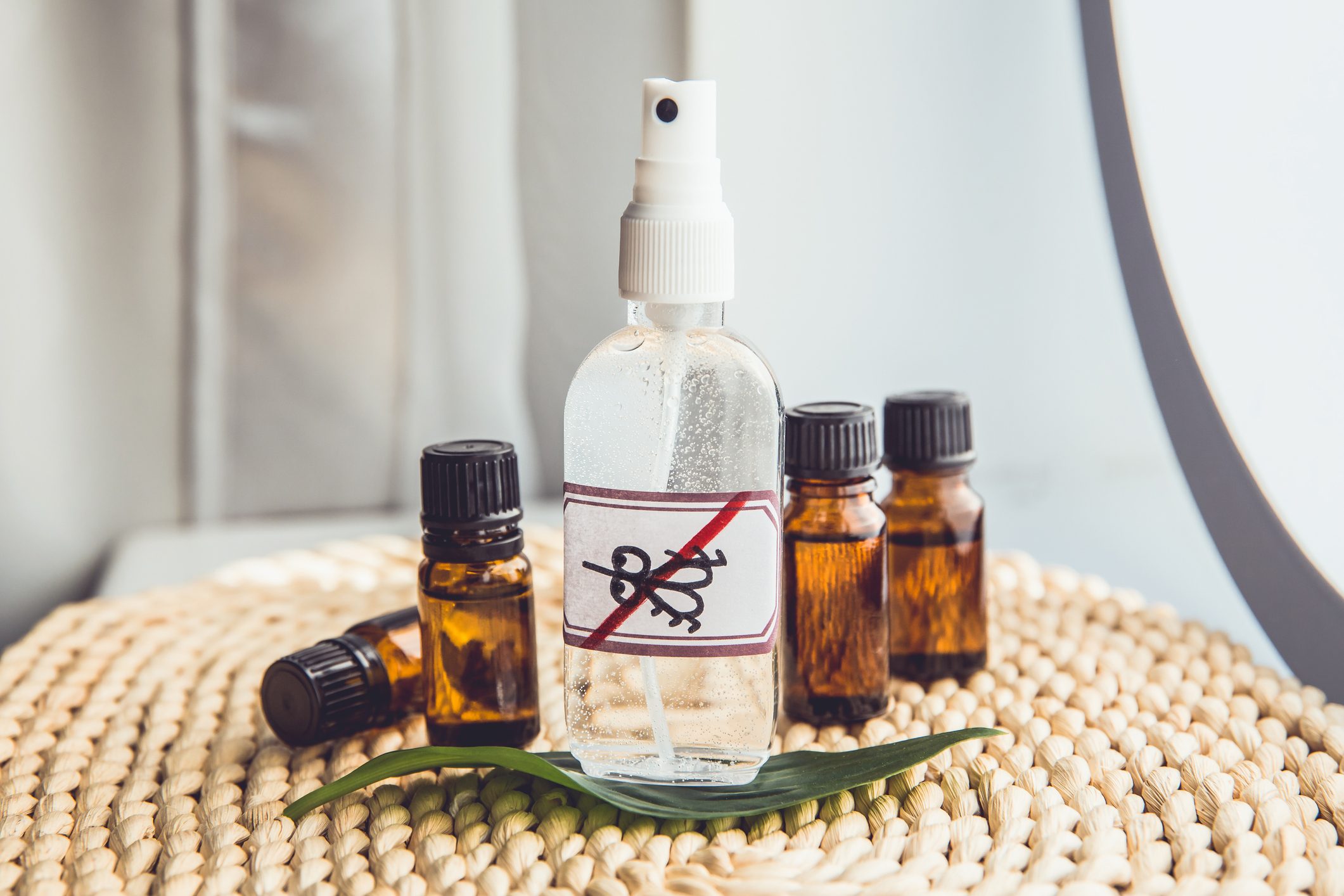 Homemade essential oil based mosquito repellent. Flat lay view of spray bottle surrounded by brown essential oil bottles on bamboo mat background.